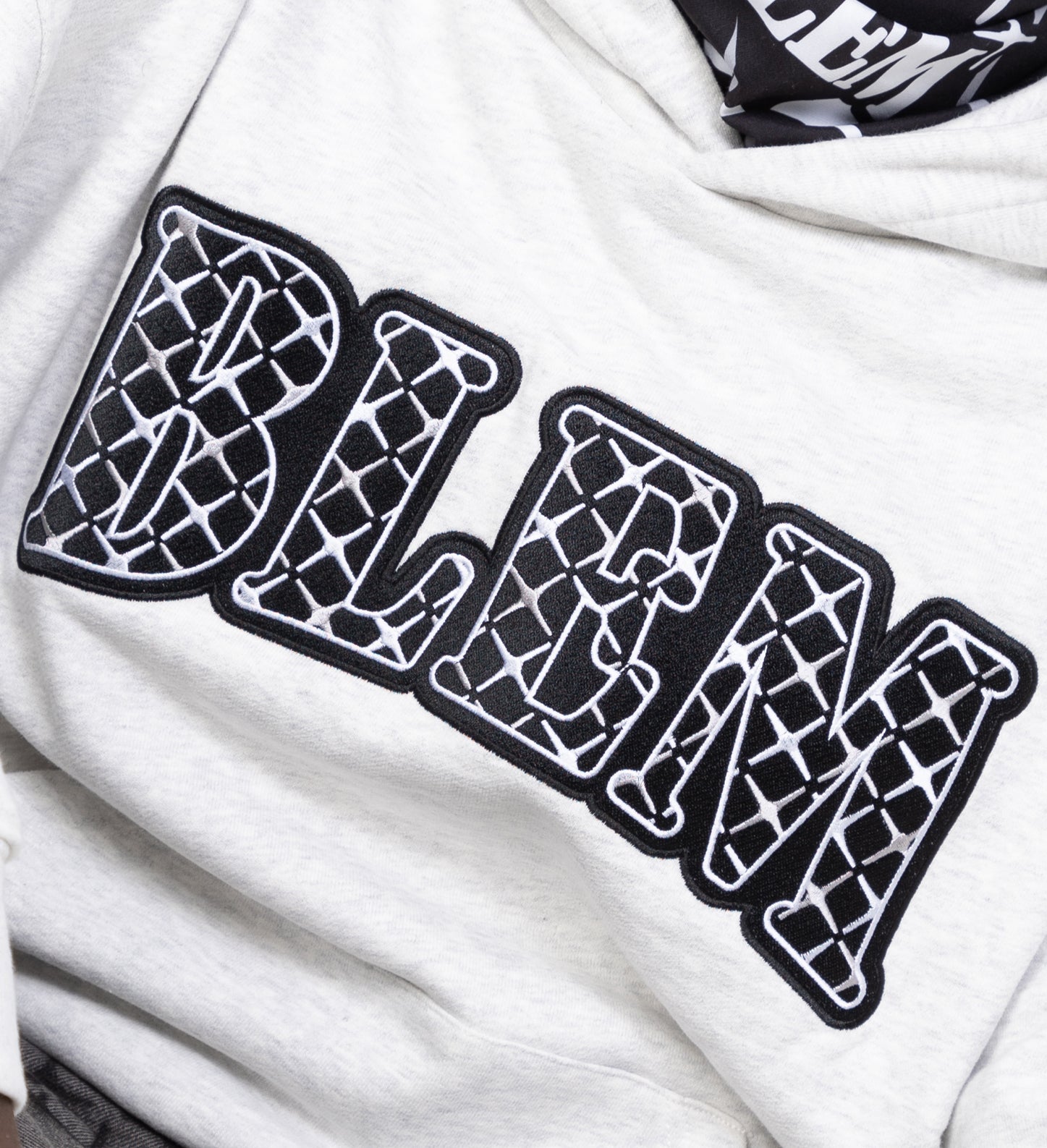 Model detail shot of a grey hoodie with embroidery spelling the word blem