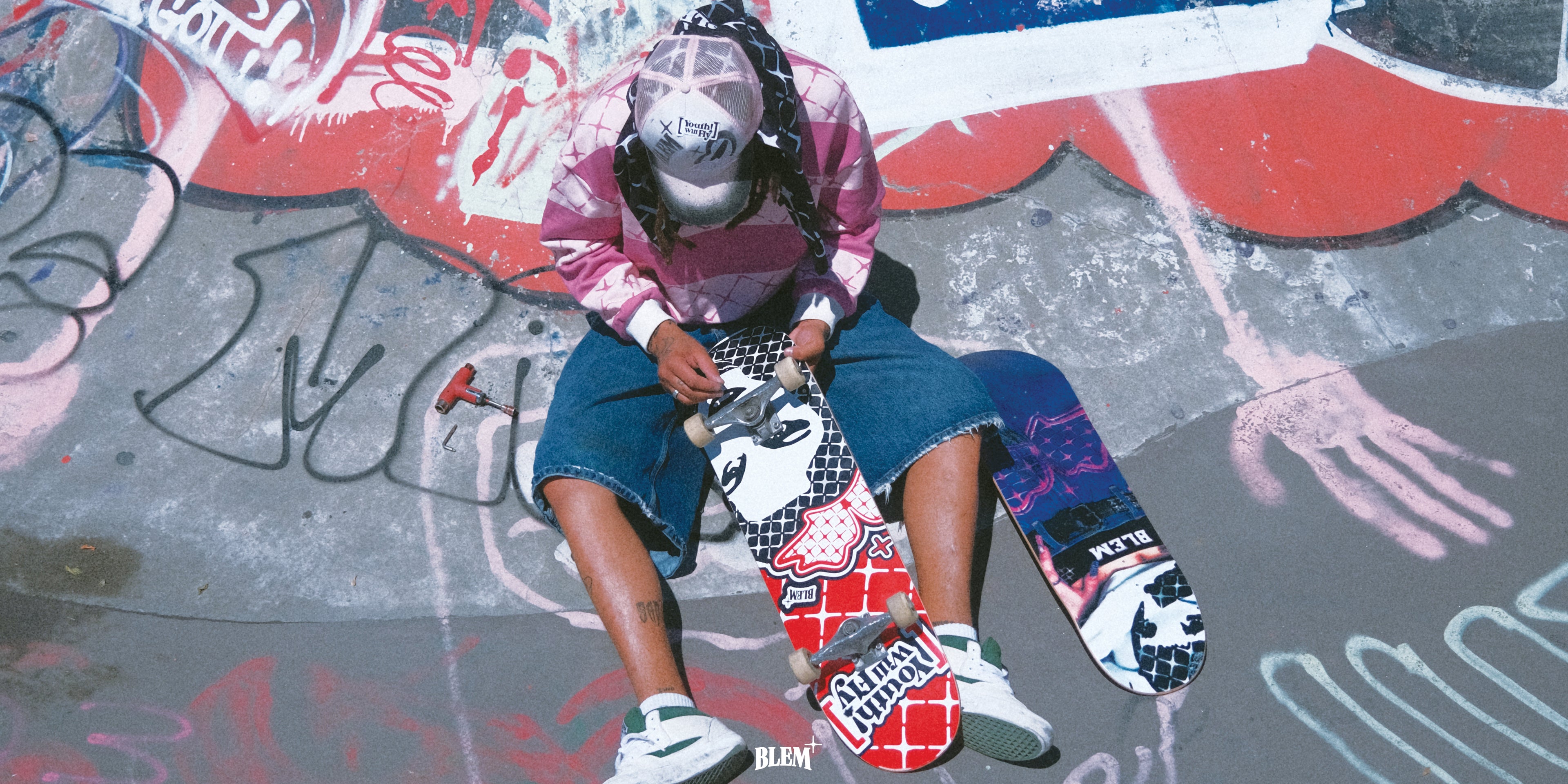 skater fixing skateboard wheels in skatepark with graffiti